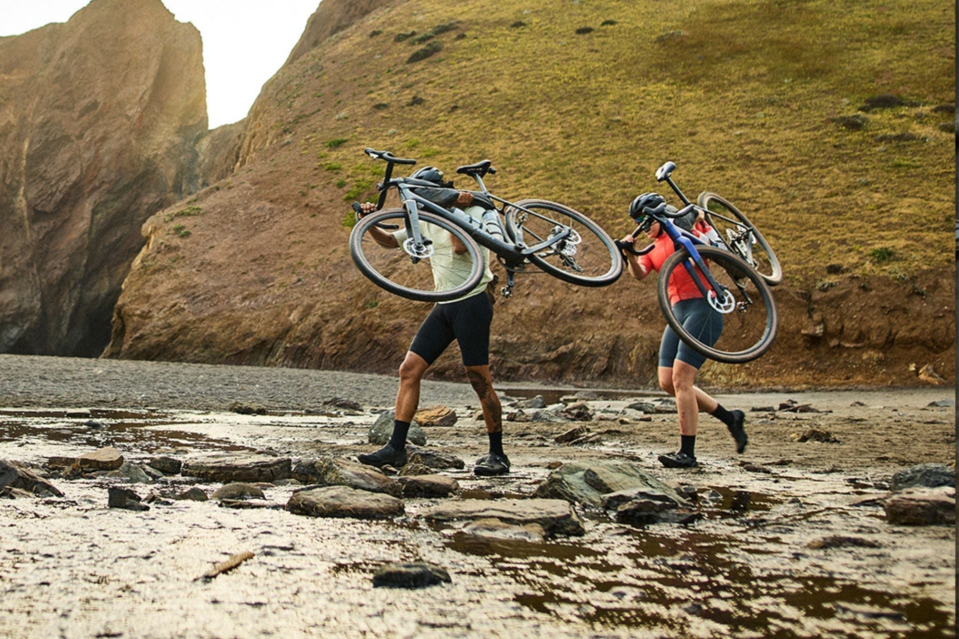 Kaksi pyöräilijää kantaa pyöriä rannalla